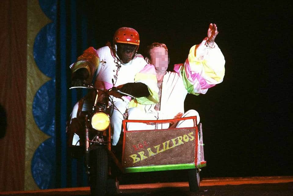 A chimpanzee drives a car with a person in it in a circus.