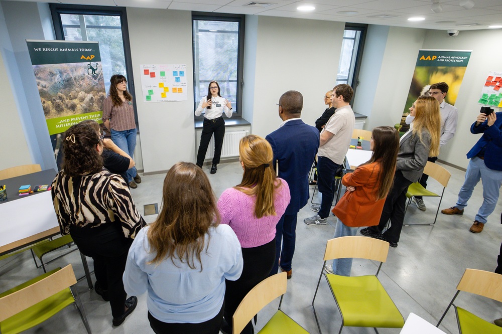 Group of people standing in a circle and looking at a paper with post its on a wall.